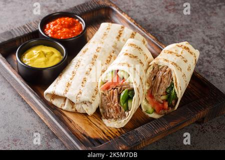 Arab Traditional Food Shawarma Rolled Sandwich mit Sauce und Gemüse Nahaufnahme auf dem Holzbrett auf dem Tisch. Horizontal Stockfoto