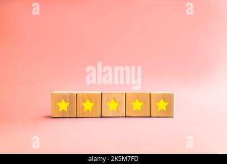 Kundenfeedback-Umfrage mit gelbem Stern auf fünf hölzernen Würfelblöcken auf pastellrosa Hintergrund mit Kopierfläche, minimalem Stil. Fünf-Sterne-Kundenprodu Stockfoto