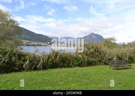 Schöne Sommerlandschaft des Flusses Adda breiten Kurs mit Bergen und große grüne Wiese mit der Holzbank im Vordergrund. Stockfoto