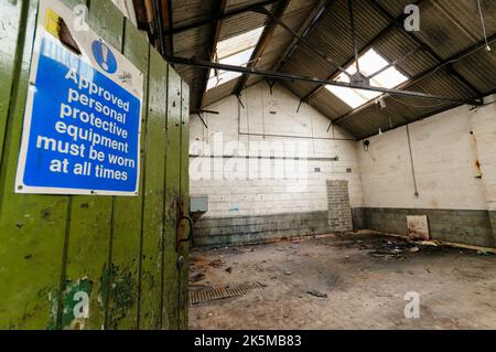 Schild mit der Aufschrift „zu jeder Zeit zugelassene persönliche Schutzausrüstung tragen“ an der Tür einer verlassenen Fabrik Stockfoto