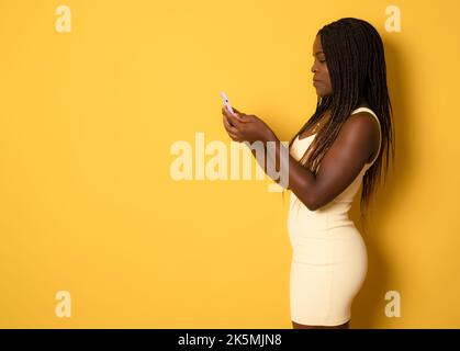 Porträt einer jungen fröhlichen afrikanischen Frau, die Smartphone für Messaging mit Freunden verwendet, Happy African Lady, die auf dem Handy textet, während sie über dem Ruder steht Stockfoto