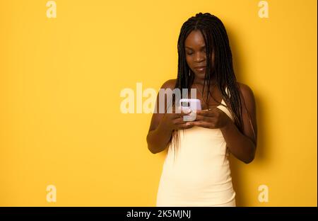 Porträt einer jungen fröhlichen afrikanischen Frau, die Smartphone für Messaging mit Freunden verwendet, Happy African Lady, die auf dem Handy textet, während sie über dem Ruder steht Stockfoto