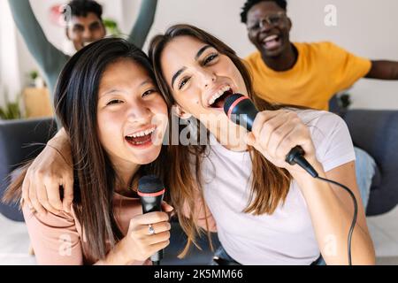 Multirassische junge Frauen, die Spaß mit Freunden haben, die Karaoke auf der Heimparty spielen Stockfoto