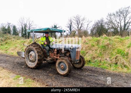 Ein Landwirt zeigt sich mit Daumen nach oben, als er einen Fordson-Traktor auf einer Spur mit einem alten Pflug fährt, Nordirland, Großbritannien Stockfoto