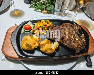 Riesiges Steak mit gebackenen Kartoffeln auf einer gusseisernen Pfanne in einem Restaurant in Mariental, Namibia Stockfoto