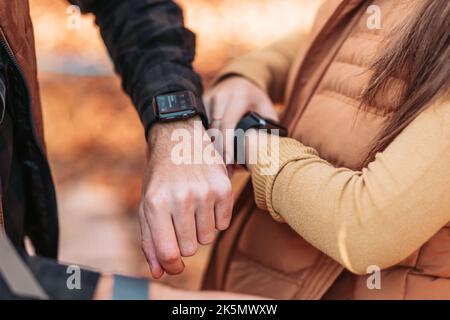Männliche und weibliche Hände mit smarten Uhren. Im Freien, Herbstfarben Stockfoto