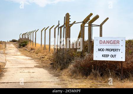 Straße mit Überresten von Betonzaunstangen mit M.O.D. Sachgefährdung Schild, Orford Ness, Suffolk, England Stockfoto