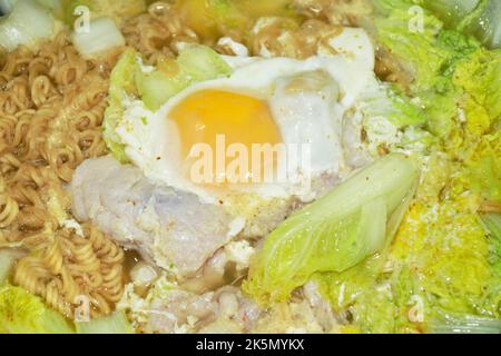 Gekochte Instant-Nudeln-Suppe mit Schweinefleisch- und Eierkohl in einem elektrischen Kochtopf in der Küche Stockfoto