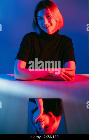 Doppeltes Gesicht. Neonlicht im Porträt. Schön vorgebend. Neugierig lächelndes Mädchen mit gelangweilt gleichgültig Gesicht Spiegelreflexion in rosa blaue Farbe leuchten isoliert Stockfoto