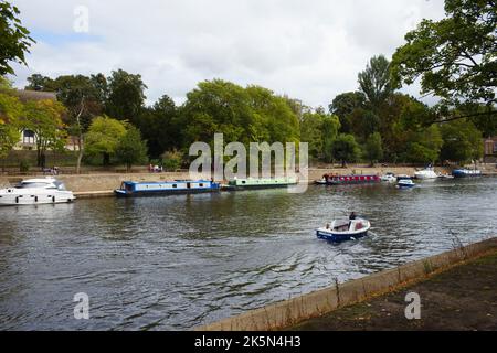 Ein kleines Tagesboot fährt an festfahrenden Schmalbooten auf dem Fluss Ouse in York vorbei Stockfoto
