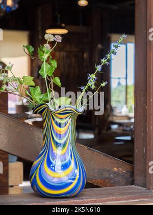 Fenster im alten Retro-Stil mit Blumen in einer bunten Glasvase. Typische Country-Szene im alten Stil. Skandinavien. Nordeuropa Stockfoto