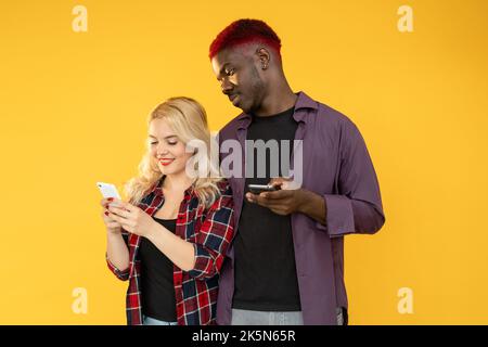 Millennials-Paar. Unterhaltung mit Gadgets. Mobiltechnologie. Surfen im Internet. Glückliche multirassische Freunde Mann Frau mit Telefon soziale Medien isoliert o Stockfoto