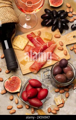 Aperitif-Set. Jamon und Cracker an Bord. Flasche Rotwein, Glas Rotwein, Feigen und Nüsse. Flach liegend. Rostiger Metallhintergrund. Stockfoto