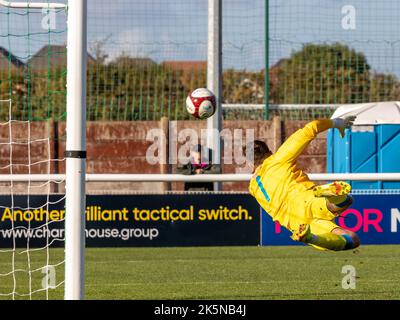 Ein Torwart taucht, um einen Schuss auf das Tor zu retten, aber verpasst den Ball Stockfoto
