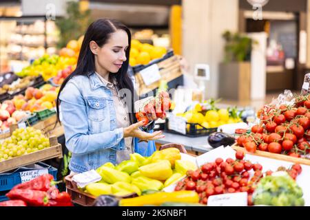 Lächelnd gut aussehende Brünette überprüft die Qualität der Bio-roten Tomaten auf dem Markt. Stockfoto