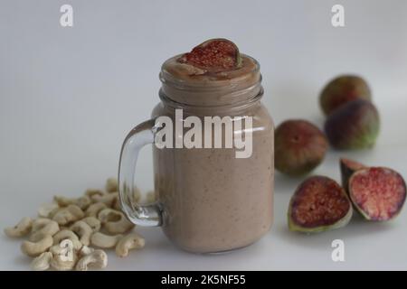 Fig Smoothie. Sommergetränk aus frischer Feige in Cashew-Milch, serviert in Glas-Smoothie-Glas. Aufgenommen auf weißem Hintergrund zusammen mit frischen reifen Feigen und cas Stockfoto