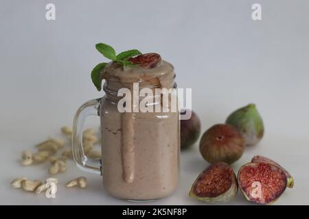 Fig Smoothie. Sommergetränk aus frischer Feige in Cashew-Milch, serviert in Glas-Smoothie-Glas. Aufgenommen auf weißem Hintergrund zusammen mit frischen reifen Feigen und cas Stockfoto