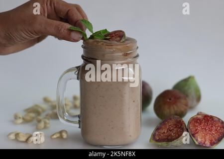 Fig Smoothie. Sommergetränk aus frischer Feige in Cashew-Milch, serviert in Glas-Smoothie-Glas. Aufgenommen auf weißem Hintergrund zusammen mit frischen reifen Feigen und cas Stockfoto