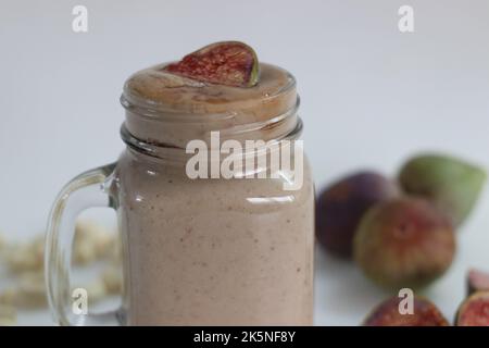 Fig Smoothie. Sommergetränk aus frischer Feige in Cashew-Milch, serviert in Glas-Smoothie-Glas. Aufgenommen auf weißem Hintergrund zusammen mit frischen reifen Feigen und cas Stockfoto