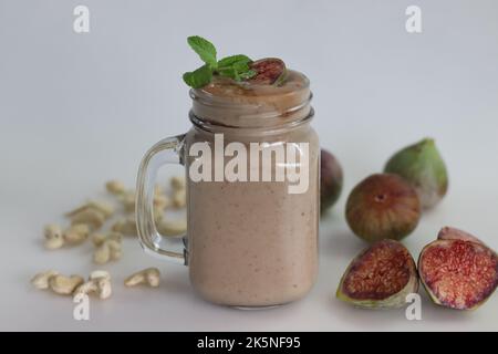 Fig Smoothie. Sommergetränk aus frischer Feige in Cashew-Milch, serviert in Glas-Smoothie-Glas. Aufgenommen auf weißem Hintergrund zusammen mit frischen reifen Feigen und cas Stockfoto