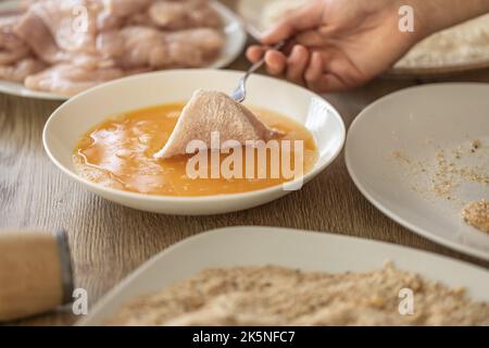 Detail der manuellen Zubereitung von Hühnerfleisch in Mehl in Eier während der Herstellung von Schnitzeln. Stockfoto