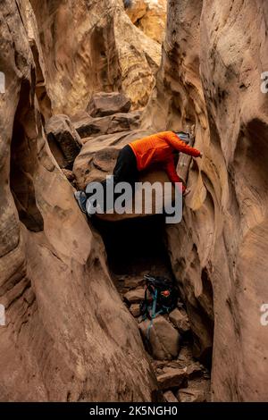 Die Frau klettert die schmalen Wände des Slot Canyon im Capitol Reef National Park hinauf Stockfoto