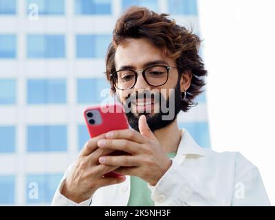 Ein junger, lächelnder italienischer Mann, der mit einem Mobiltelefon in einer Stadt chattet Stockfoto