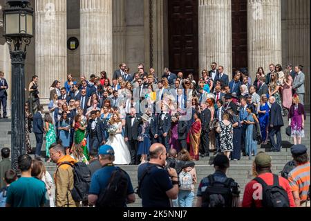 LONDON - 21. Mai 2022: Braut, Bräutigam und Gäste posieren auf den Stufen der St. Paul's Cathedral, während Touristen zusehen Stockfoto