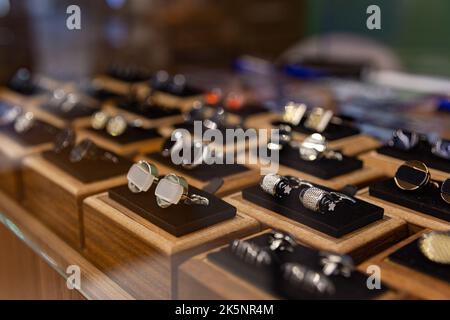 Boxen mit Manschettenknöpfen im Regal in der Boutique. Set aus schönen Manschettenknöpfen aus Platin oder Gold, verschiedene Formen. Manschettenknöpfe in Holzkisten auf schwarzem Samt pa Stockfoto