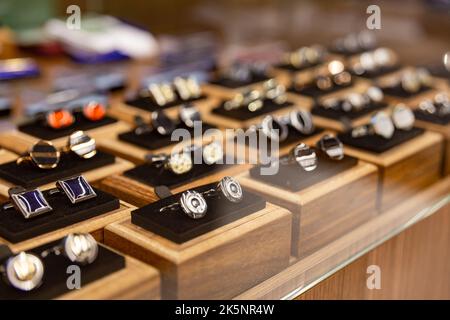 Boxen mit Manschettenknöpfen im Regal in der Boutique. Set aus schönen Manschettenknöpfen aus Platin oder Gold, verschiedene Formen. Manschettenknöpfe in Holzkisten auf schwarzem Samt pa Stockfoto