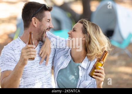 Lächelnde Touristen klirren Bierflaschen auf dem Campingplatz Stockfoto