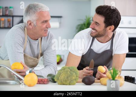 Ein erwachsener Sohn und ein älterer Vater kochen drinnen Stockfoto