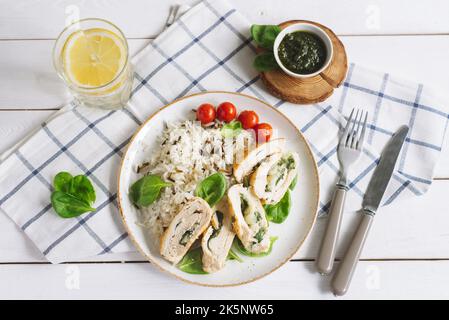 Hühnerfilet Rollen mit Spinat, auf einem Bett aus Langkornreis, garniert mit frischen Spinatblättern und Kirschtomaten. Hausgemachtes Abendessen auf einem Check-in Stockfoto