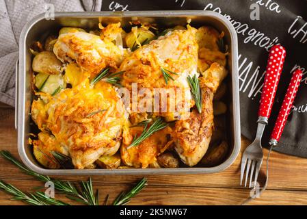 Hähnchenschenkel mit Käse auf Kartoffelkeilen und Rosmarin gebacken. Auflaufform bügeln. Blick auf das heiße Gericht von oben. Stockfoto