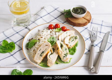 Hühnerfilet Rollen mit Spinat, auf einem Bett aus Langkornreis, garniert mit frischen Spinatblättern und Kirschtomaten. Hausgemachtes Abendessen auf einem Check-in Stockfoto