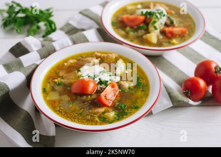 Suppe mit Huhn, Linsen und saurer Rahm. Zwei große Teller Gemüsesuppe mit Hühnerbrühe, garniert mit großen Tomatenscheiben und gehackten Kräutern Stockfoto