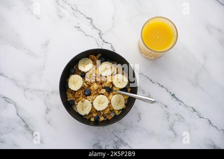 Gesundes Frühstück mit Vollkornprodukten mit Milch, Heidelbeeren, Bananen und Orangensaft auf der Arbeitsplatte aus weißem Marmor. Stockfoto