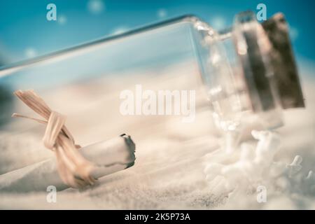 Nahaufnahme einer kleinen Glasflasche mit einer Papiernachricht. Die Flasche steht am Strand Stockfoto