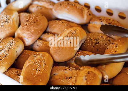 Viele frisch gebackene Brötchen in Plastikbox mit Zange, Nahaufnahme, Bäckerei. Stockfoto