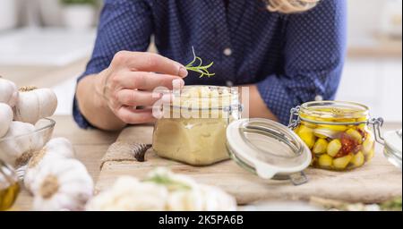 Detail einer Frau, die einen Zweig Rosmarin auf ein Glas voller zerdrückter Knoblauchpaste setzt. Stockfoto