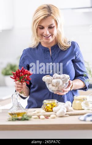 Frau hält eine Schüssel mit frischem Knoblauch und Chilischoten, die in der Küche Konfitüren zubereitet. Stockfoto