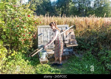 Borovichi, Russland - 13. September 2022: Junge attraktive Frau in der Nähe des Dorfes hölzernen Brunnen im Sommer sonnigen Tag Stockfoto