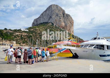 Touristen, die nach einem Tagesausflug nach Benidorm in Calpe ein Boot besteigen. Penyal d'IFAC Natural Park, ein riesiger Kalksteinausbiss, liegt im Hintergrund Stockfoto