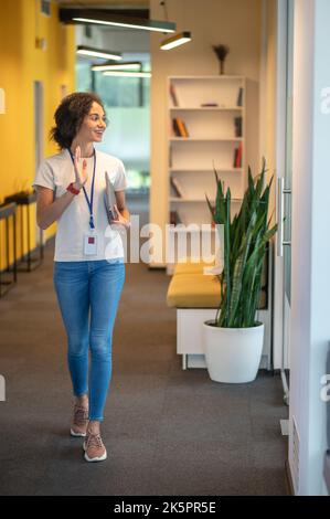 Nette Büroangestellte winkt ihren Kollegen zu, während sie an ihrem Zimmer vorbeikommt Stockfoto