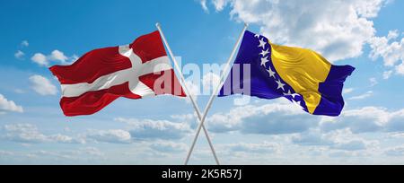 Zwei gekreuzte Flaggen Bosnien und Herzegowina und Dänemark winken im Wind bei bewölktem Himmel. Konzept der Beziehung, des Dialogs, des Reisens zwischen zwei Ländern. Stockfoto