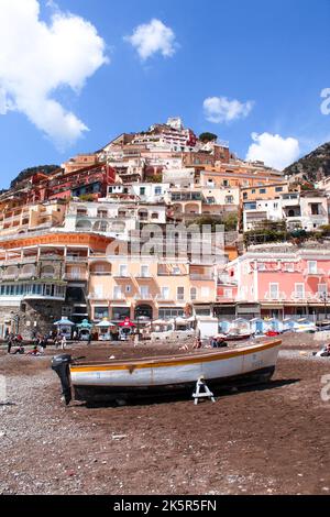 Eine vertikale Aufnahme eines alten Bootes am Strand von Positano mit bunten Häusern im Hintergrund Stockfoto