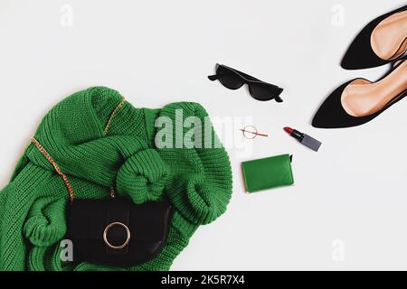 Modisches Outfit flach liegend. Grüner Strickpullover, Schuhe, Sonnenbrillen und andere Accessoires, Draufsicht Stockfoto
