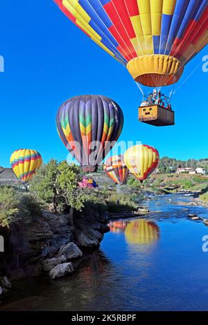 Bunte Heißluftballons schweben während der Colorfest Heißluftballonfahrt 2022 in Pagosa Springs, Colorado, USA, über dem San Juan River. Stockfoto