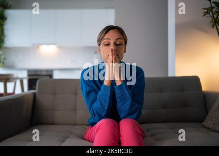 Traurige Frau im blauen Pullover sitzt auf einem bequemen Sofa und leidet zu Hause an Herbstdepression Stockfoto