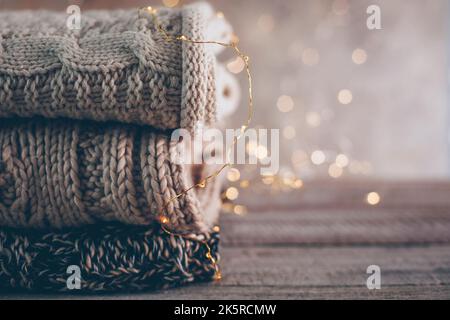 Gemütliche Strickpullover im Winter oder Herbst und Girlande-Lichter auf Holzhintergrund. Warmes, Gemütliches Konzept. Speicherplatz kopieren Stockfoto